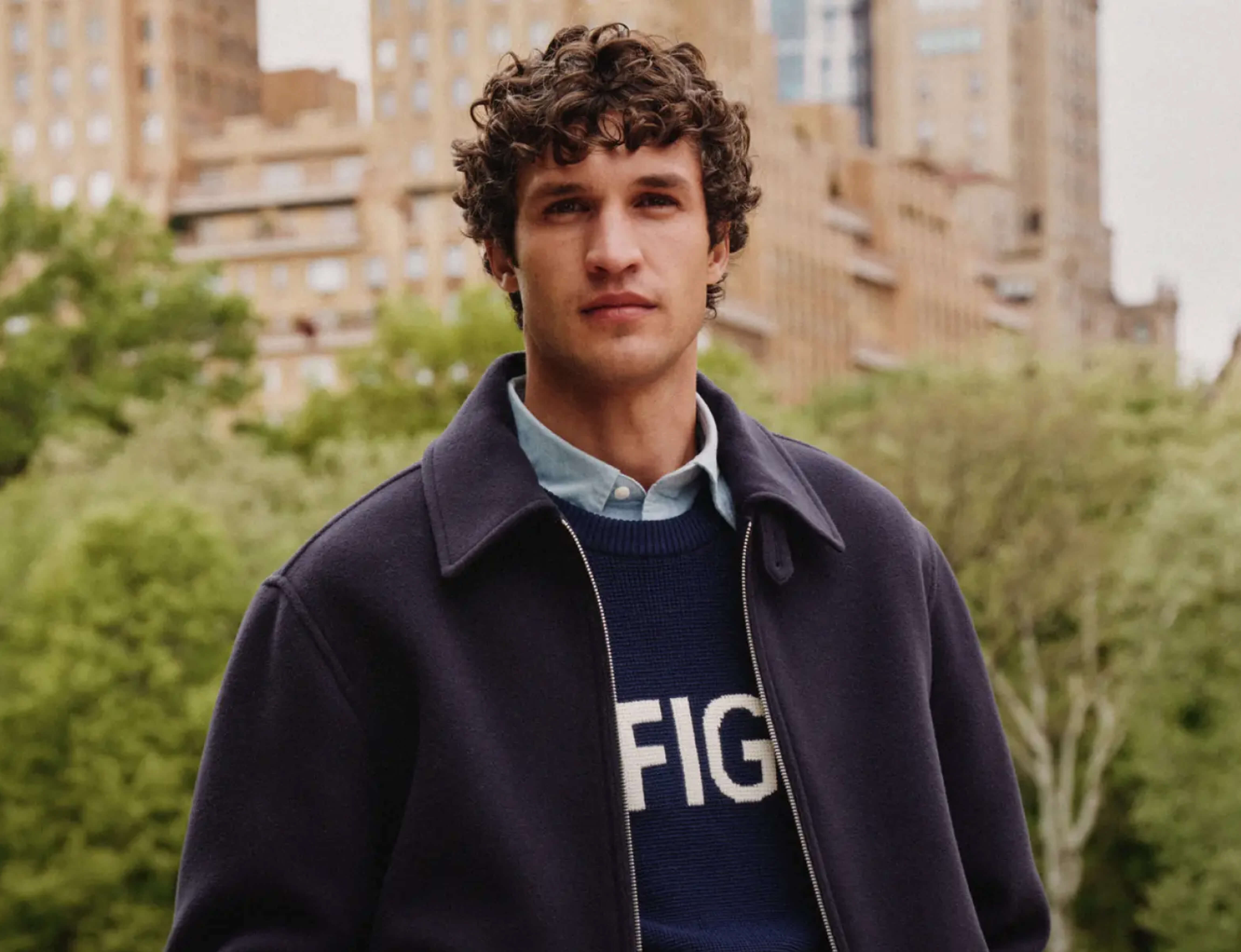 Homme portant un polo rayé blanc et bleu marine Tommy Jeans, assis devant un pont à New York